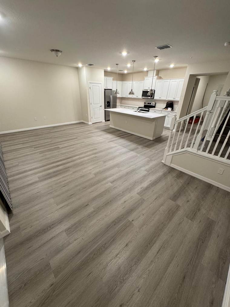 Gray vinyl plank floor across a living area with white kitchen